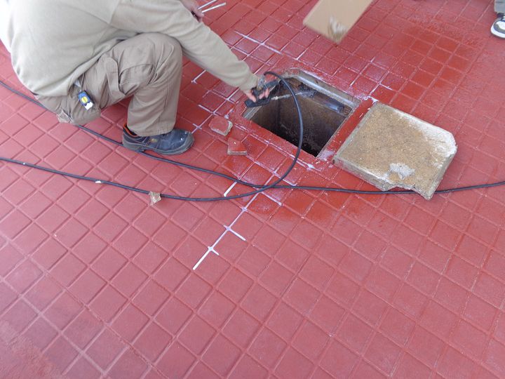 Técnico agachado revisando un registro en un suelo de baldosas rojas