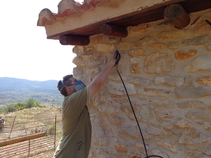 Técnico con mascarilla tratando un muro de piedra y su alero de madera